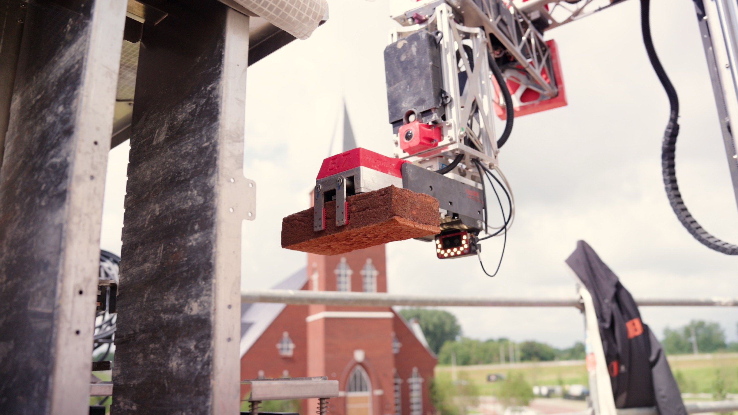 A Monumental robot placing a brick with millimeter precision, a historic church behind it